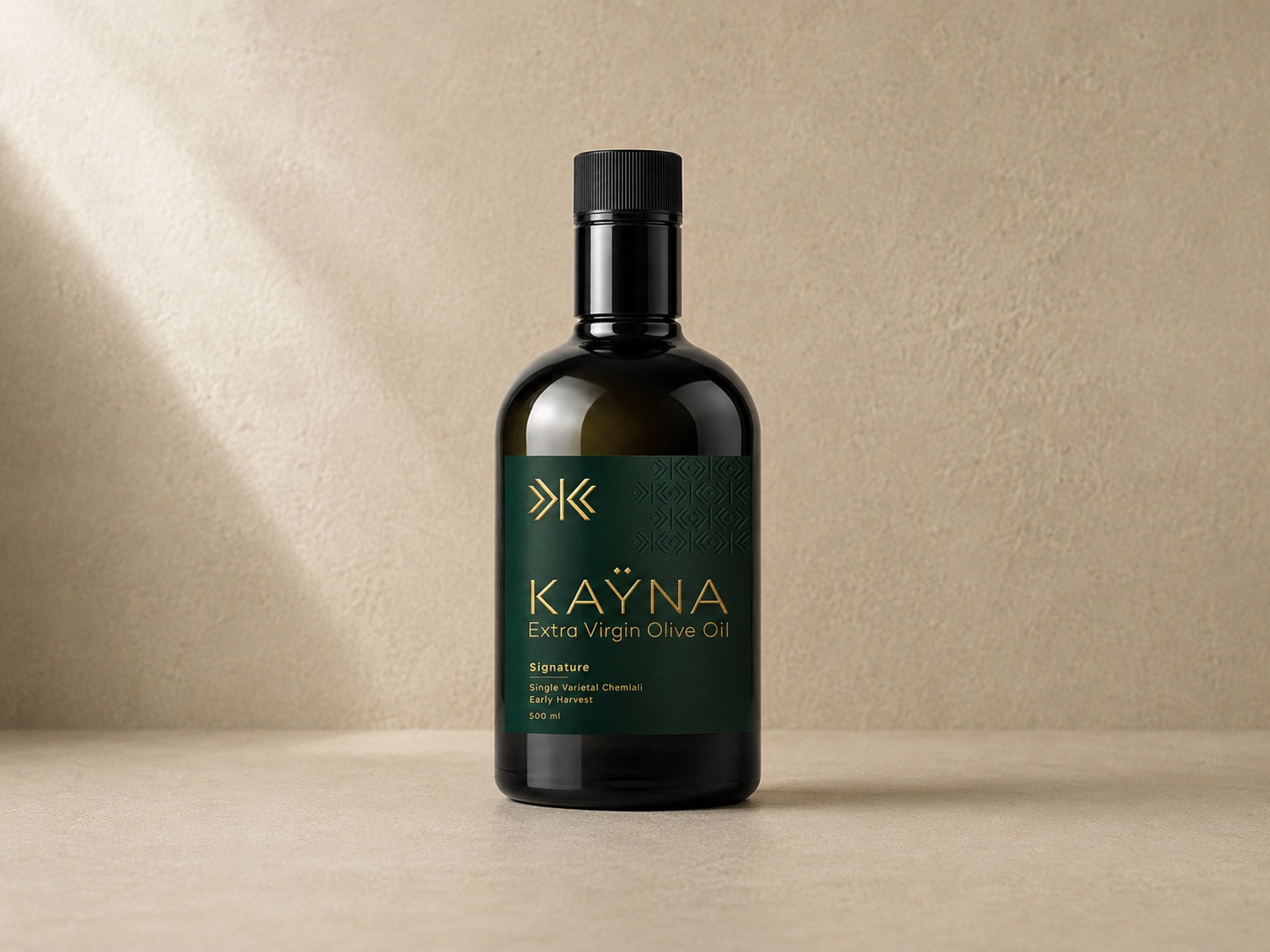 Bouteille KAŸNA Signature, huile d'olive extra vierge premium, posée sur une pierre claire dans la lumière méditerranéenne