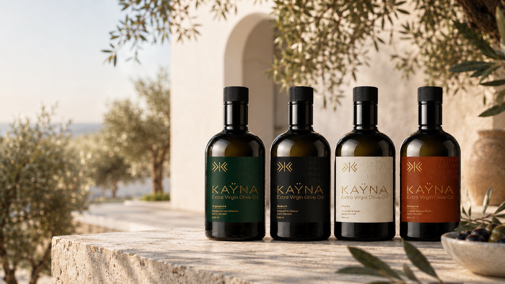 Les quatre créations KAŸNA — Signature, Robust, Fruity, Réserve — posées sur un muret de pierre, entre les oliviers